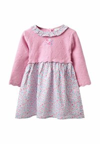 Top rosa lavorato a maglia con maniche lunghe e colletto a ruffles, abbinato a una gonna in tessuto con motivo floreale nei toni di blu, rosa e bianco.