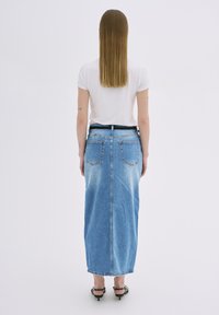 Denim maxi suknja svijetlo plave boje, s izblijedjelim detaljima i dva stražnja džepa. Uparena s običnom bijelom majicom i crnim petama.