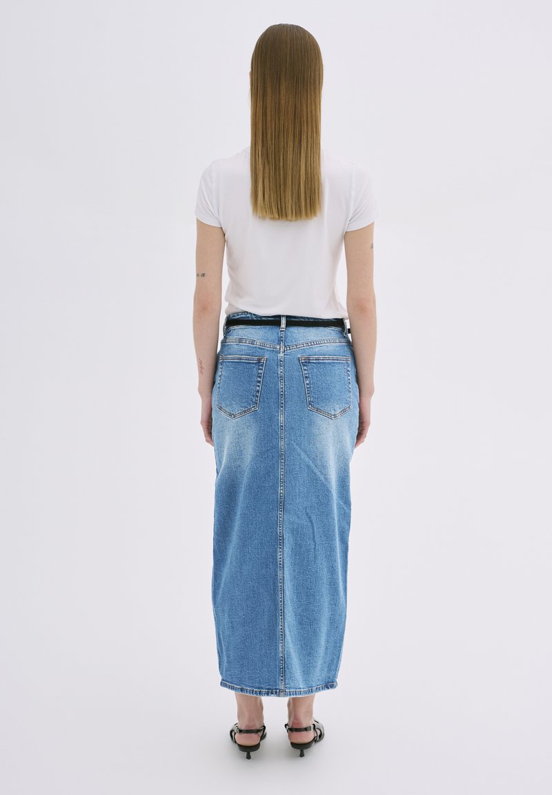 Denimowa spódnica maxi w jasnoniebieskim odcieniu, z wyblakłymi detalami i dwiema tylnymi kieszeniami. Połączona z gładką białą koszulką i czarnymi szpilkami.