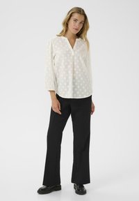 White blouse with polka dot texture, mandarin collar, and three-quarter sleeves, paired with black flared trousers and black shoes.
