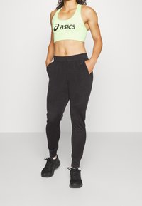 Zwarte slim-fit joggers met zijzakken, gecombineerd met een neon groene cropped sportbh met een zwart logo. Zwarte sportschoenen maken de look compleet.