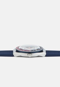 Navy rubber strap watch with a round silver case, domed glass, and a multicolored bezel featuring red, blue, and white accents.