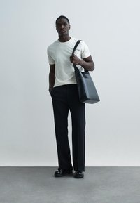 Saco tote preto, t-shirt bege claro, calças pretas, sapatos pretos brilhantes. Design simples com corte reto, linhas limpas e detalhes mínimos.