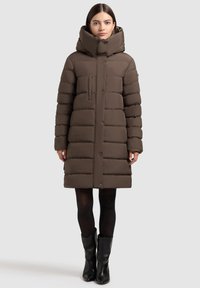 Pruun paks soojajakk kõrge kraega, nööpidega ees, horisontaalse õmblusega, rinnatasku ja pikkade varrukatega. Kandmiseks koos põlviksaabastega.