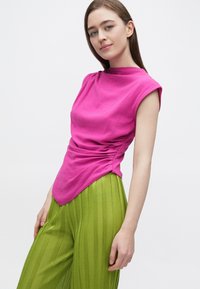 Fukszia rövid ujjú felső oldalán összehúzott részlettel, zöld, pliszírozott, bő szárú nadrággal párosítva. Sima textúra, testhez simuló sziluett, modern kialakítás.