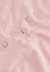 Ružičasta pamučna majica sa istaknutim, zlatnim metalnim natpisom "BAKER" i "by TED BAKER" u glatkom dizajnu, s okruglim izrezom.