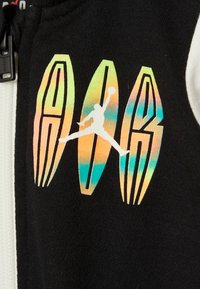 Černý fleecový zip-up s barevným gradientním logem, na kterém je skákající postava. Design obsahuje výrazné písmo a hladkou texturu.