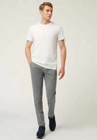 Vitt bomullströja med korta ärmar och en liten logotyp, i kombination med grå byxor. Outfitten fulländas med marinblå sportskor.