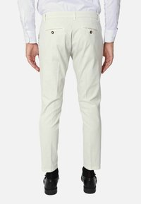 Pantaloni bianchi in cotone con una vestibilità slim, dotati di tasche posteriori con bottoni scuri, abbinati a scarpe nere e calze visibili.