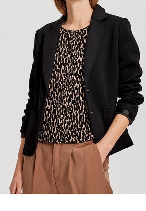 Blazer nero con tre bottoni, indossato su una top leopardato in beige e nero. Pantaloni alta vita marroni. Tessuto morbido e design strutturato.