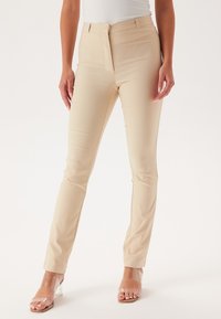 Pantaloni beige aderenti con una texture liscia, dotati di una vita standard, zip frontale e dettagli di design sottili.