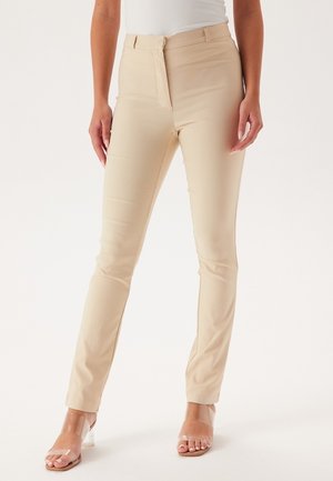Béžové slim-fit kalhoty s hladkou texturou, mají standardní pas, přední zip a jemné designové detaily.