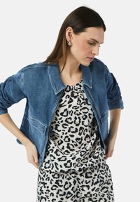 Veste en jean avec un col, de couleur bleu clair, à manches longues, portée sur un haut à manches courtes imprimé léopard beige et noir.