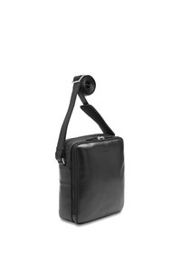 Black leather rectangular crossbody bag with zip closure and adjustable shoulder strap coiled at top against white background.
