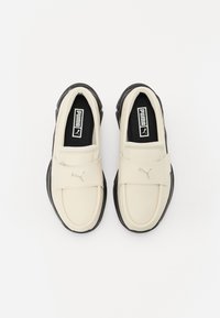 Bottines couleur crème avec une semelle en caoutchouc noire. Dotées d'un matériau supérieur lisse et d'un logo Puma en argent sur la sangle.
