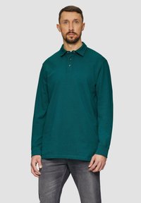 Polo z długim rękawem w kolorze teal z trzema guzikami, wykonane z teksturowanej tkaniny, w połączeniu z szarymi dżinsami, charakteryzującymi się luźnym fasonem i standardowymi mankietami.