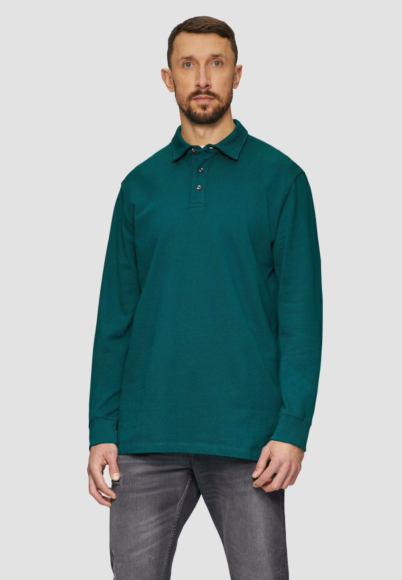 Polo z długim rękawem w kolorze teal z trzema guzikami, wykonane z teksturowanej tkaniny, w połączeniu z szarymi dżinsami, charakteryzującymi się luźnym fasonem i standardowymi mankietami.
