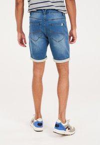 Shorts de mezclilla en azul claro, con dobladillos enrollados, bolsillos traseros con detalles de costura, combinados con zapatillas deportivas en gris y azul.