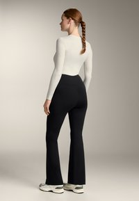 Form-fitting long-sleeve top in light cream, paired with high-waisted black flared pants. Minimalist design with smooth texture.