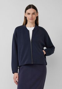 Navyblaue Bomberjacke aus einem weichen Material mit Reißverschluss vorne, Seitentaschen und gerippten Bündchen. Hat einen lässigen Schnitt und einen runden Ausschnitt.