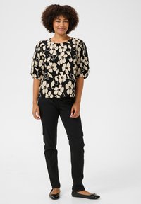 Haut noir à motif floral beige, manches courtes bouffantes, associé à un pantalon noir et des chaussures plates. Design simple en tissu texturé.