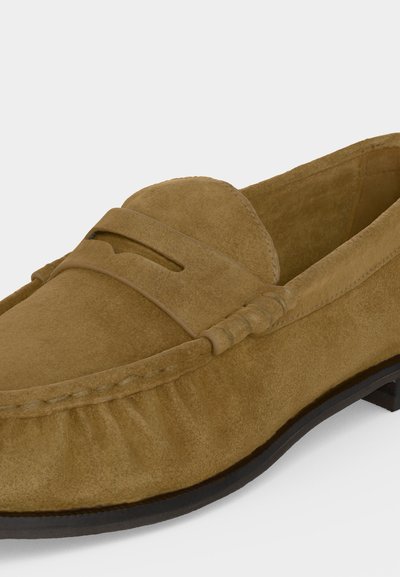 Mocassin en daim marron clair avec surpiqûres mocassin, une bride penny sur le dessus et une semelle extérieure noire.
