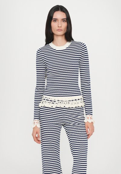 Bluza tricotată cu dungi și pantaloni în nuanțe de bleumarin și alb, caracterizată printr-o dantelă rafinată la manșete și margine; mânecile lungi și designul ajustat subliniază silueta.