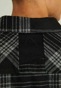 Colletto di camicia a quadri in tonalità nere e grigie, realizzato in un materiale testurizzato simile alla lana e con un design a schiena aperta, dotato di un'etichetta tessuta.