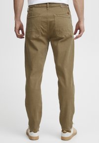 Pantaloni in cotone color khaki con una vestibilità dritta, due tasche posteriori e un piccolo etichetta del marchio sulla vita. Indossati con sneakers bianche.