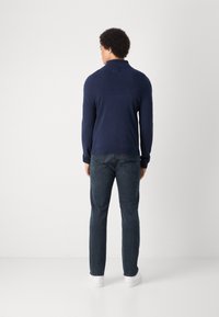 Marinblå tröja med krage, parat med mörka jeans. Tyget ser slätt och figurnära ut, med långa ärmar och en diskret design på kragen.