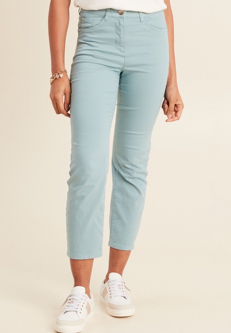 Lichtblauwe enkellange broek van katoen, met een aansluitend ontwerp, vijf zakken en een enkele sluiting met een knoop aan de voorkant. Gepaard met witte sneakers.