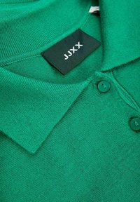 Grön polo skjorta med en texturerad stickning, en klassisk krage, två knappstängningar och en svart etikett med "JJXX"-logotyp.