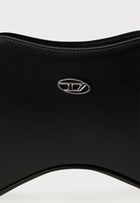 Czarna skórzana kopertówka o gładkiej fakturze, zakrzywionym kształcie i metalicznym akcentem z logo. Charakteryzuje się eleganckim, minimalistycznym stylem.