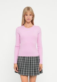 Haut à manches longues côtelé rose pâle associé à une jupe à carreaux noir et blanc. L'ensemble présente une encolure ronde et s'ajuste près du corps.