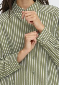 Persona che allaccia il polsino di una camicia a maniche lunghe a righe verticali verdi e bianche.
