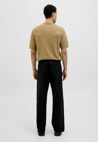 Trumpas rankovėmis, alyvuogių žalios spalvos marškiniai su apvalia iškirpte, derinami su laisvai krentančiais juodais kelnėmis. Audinys atrodo minkštas, su minimaliu dizaino akcentu.