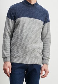 Šedý a námořnicky modrý vzorovaný pletený svetr s kulatým výstřihem, texturovanými částmi a žebrovanými manžetami a lemem. Nošený s tmavými džínami z denimu.