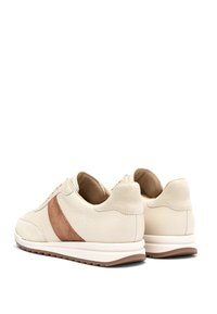 Kreemvärvilised nahast jooksujalatsid pruuni sametist külgriiviga, pehme krae ja valge kummist tallaga, nähtavad tagant ja küljelt valgel taustal.