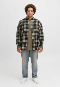 Sort og hvid ternet button-up skjorte over en khaki T-shirt, parret med falmede lyseblå jeans og hvide sneakers.