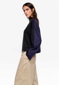 Zwart en marinekleurige kleurgebroken sweatshirt met hoge kraag en lange mouwen, gecombineerd met beige wijde pantalon. Zachte stof, relaxte pasvorm.