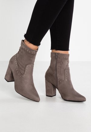 Stivaletti alla caviglia in suede grigio con punta affilata e tacco a blocco, caratterizzati da dettagli decorativi in borchie e una cerniera laterale per la chiusura.