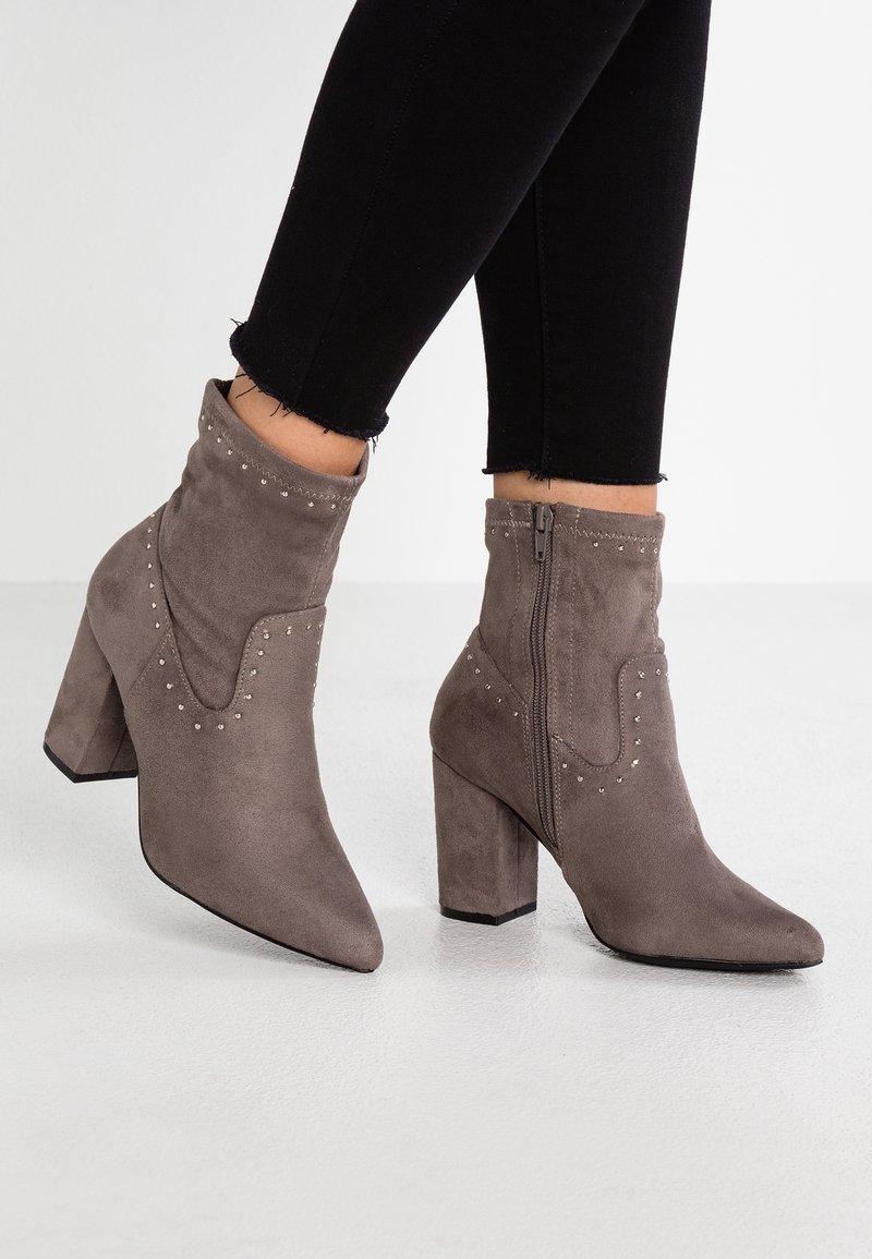Botines de ante gris hasta el tobillo con puntera puntiaguda y tacón cuadrado, con acentos decorativos de tachuelas y un cierre de cremallera lateral.