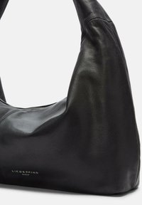 Borsa a tracolla in pelle nera con una texture liscia, forma hobo, silhouette curvata e un discreto dettaglio di branding. Chiusura con zip nella parte superiore.