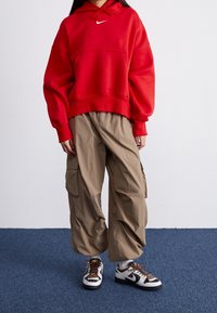 Röd överdimensionerad sweatshirt med framficka och dragstringshuva, tillsammans med beige cargobyxor med sidofickor och svarta och vita sneakers.