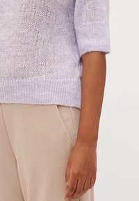 Ljuslila stickad tröja med lös passform, korta ärmar och ribbad nederkant, kombinerad med beige högmidjade byxor.