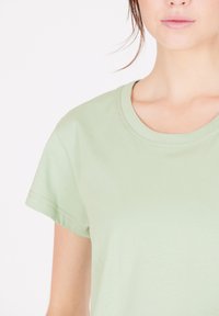 Ljust grön bomull t-shirt med korta ärmar och rundad halsringning. Slät textur, minimala sömdetaljer. Inga synliga mönster eller grafiker.