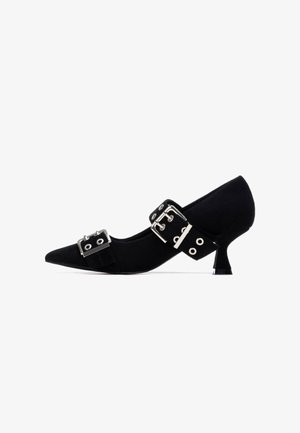 Zapato pump de tacón alto de ante negro con punta puntiaguda, que presenta dos tiras anchas adornadas con hebillas plateadas y ojales, y un tacón afilado.