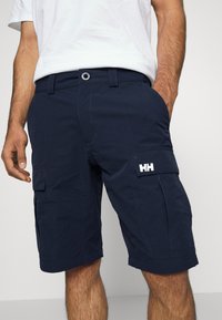Shorts cargo bleu marine en tissu résistant, avec deux poches latérales et une poche plaquée sur la cuisse ornée d'un logo blanc.