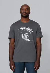 Grijze katoenen t-shirt met een witte grafiek van een astronaut die op een golf surft. Korte mouwen en een ronde halslijn. Soepele textuur.