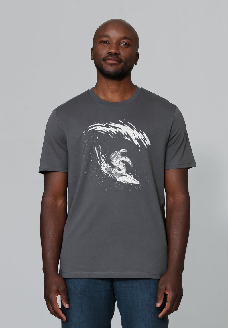 Grijze katoenen t-shirt met een witte grafiek van een astronaut die op een golf surft. Korte mouwen en een ronde halslijn. Soepele textuur.